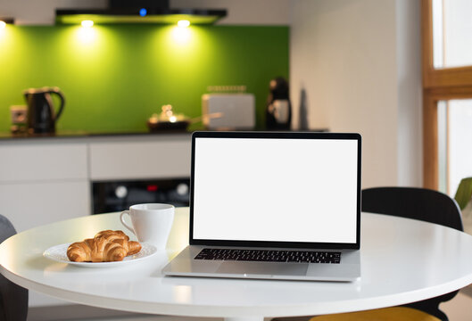 Laptop computer with empty blank mockup screen over modern white kitchen interior. Advertisement, e-learning, shopping online, web site design, technology, home office concept.