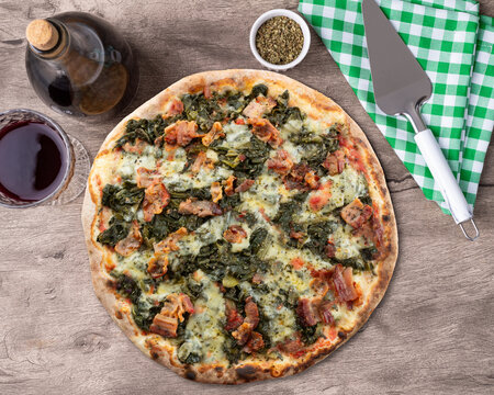 Endive, bacon and mozzarela pizza over wooden table with wine, oregano and spatula
