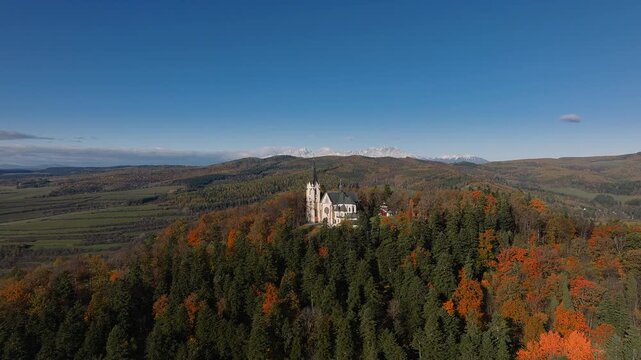 Levoca, Slovakia - 4K Flying by Basilica of the Visitation of the Blessed Virgin Mary on a sunny autumn day with colorful autumn foliage by the High Tatras mountains and blue sky at background