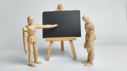 Corporate discipline and workplace evaluation concept with a wooden mannequin pointing at a blank blackboard while another stands in a sad pose. © Dhiyaafiq