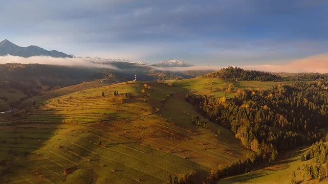 Osturna, Slovakia - 4K Flying by the High Tatras Mountains near the village of Osturna on a sunny, foggy autumn day at sunrise. Warm colors, autumn foliage, blue sky