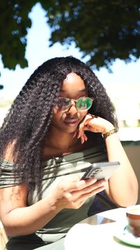 Young woman using and talking on a mobile phone in a cafe outdoors on a sunny day