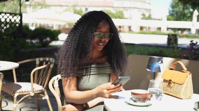 Young woman using and talking on a mobile phone in a cafe outdoors on a sunny day