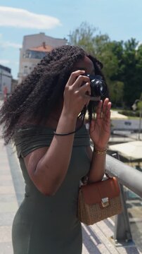 Young black woman traveler taking a photo with a camera on the street on a sunny day in Europe, Nis, Serbia