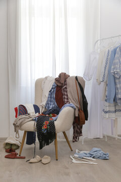 Armchair covered with clothes, used as a clothing drop zone, representing everyday clutter, postponed tidying, busy daily routines, overconsumption, and the challenge of staying organized