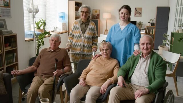 Portrait of diverse group of seniors with disabilities and young female nurse smiling at camera in nursing home. Video for marketing assisted living facilities