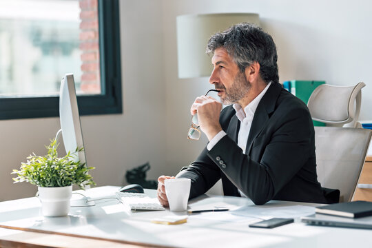 Mature elegant businessman working on a computer while drinking coffee in the office