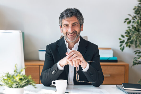 Smiling elegant businessman working on a computer while looking at camera in the office