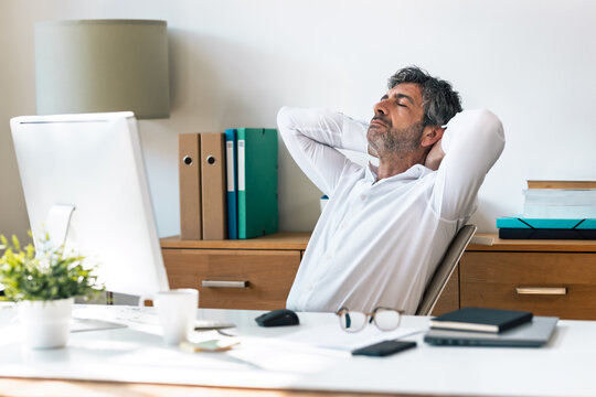 Exhausted businessman stretching while working on a computer in the office