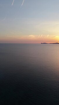 Vertical aerial reveal of Capo Caccia at sunset with smooth left to right drone pan revealing dramatic limestone cliffs and the Mediterranean Sea in golden hour light.