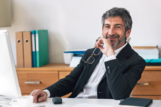 Smiling elegant businessman working on a computer while looking at camera in the office