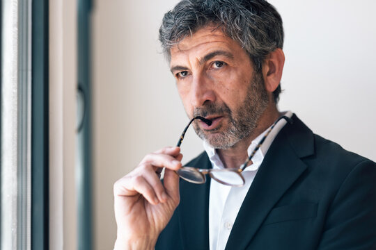 Elegant handsome businessman thinking while looking forward standing next to the window at the office.