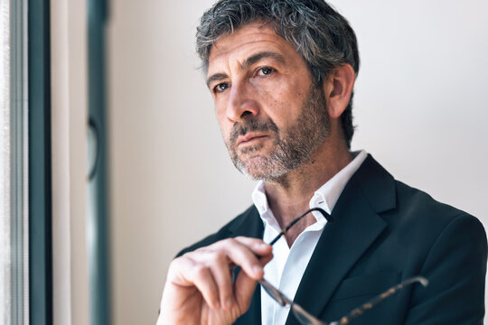Elegant handsome businessman thinking while looking forward standing next to the window at the office.