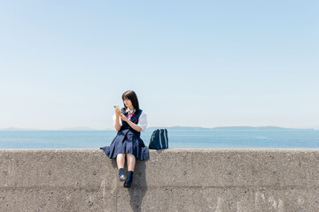 Fototapeta premium 海辺の防波堤でスマートフォンを見る女子高校生