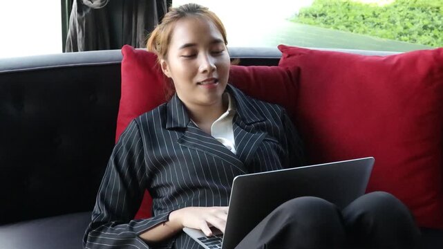 young asian businesswoman working on sofa with bad slouching posture at home during daytime, risking back pain from prolonged sitting
