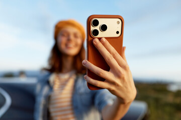 Fototapeta premium Cheerful woman outdoors taking a selfie with a warm phone glow, sunlit moment, relaxed posture, soft breeze, natural colors, lush greenery background, candid smile