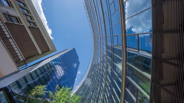 Time-lapse looking up at downtown high-rise glass office towers, financial district skyscrapers, modern urban architecture, sunny day, blue sky clouds