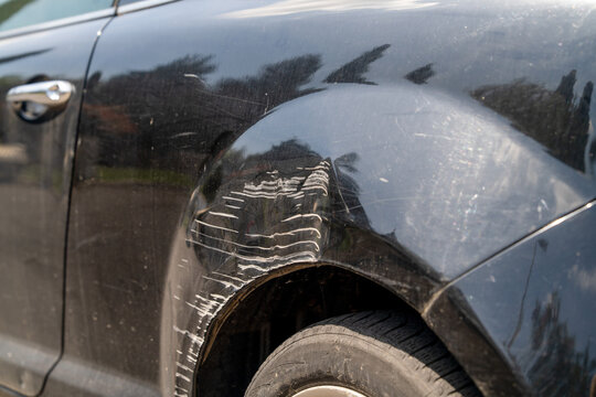 Damaged black car panel with tire mark scratch near the wheel arch, automotive accident detail, vehicle repair documentation