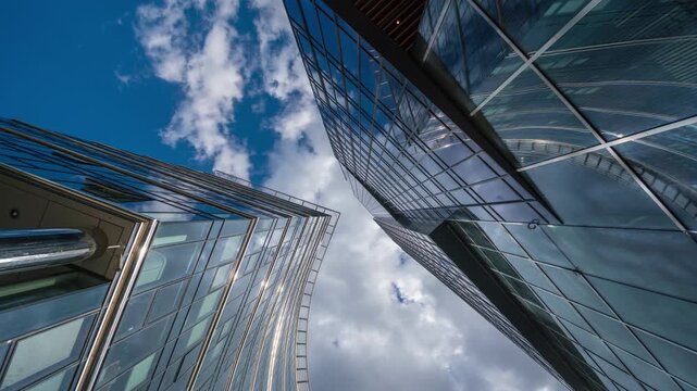 Low angle wide shot time-lapse of downtown glass skyscrapers and high-rise office buildings on sunny day, financial district modern architecture against blue sky and white clouds