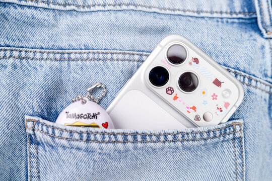 Bar, Montenegro: February 6, 2026: Iphone 17 pro in a floral case with a Tamagotchi keychain charm in a blue denim jeans pocket, fun tech accessory lifestyle