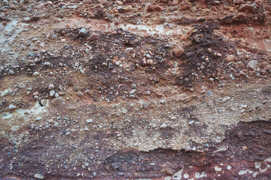 Natural conglomerate rock texture with mixed gravel and pebbles embedded in red sediment, abstract geological background.