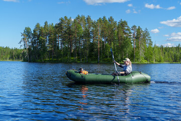 Young woman paddling an inflatable green packraft on a calm lake with her small dog in a life jacket during a sunny summer day © Alex Barera