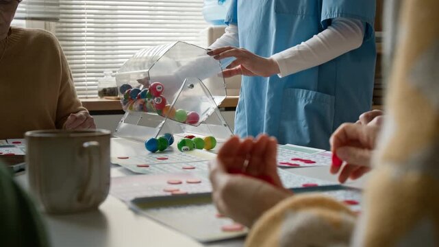 Side view close up shot of nurse spinning bingo drum for seniors playing board game in retirement home. Video for promoting assisted living and elderly care
