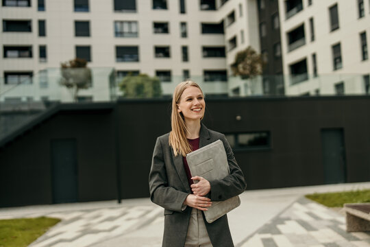 Professional woman smiling holding laptop bag in city