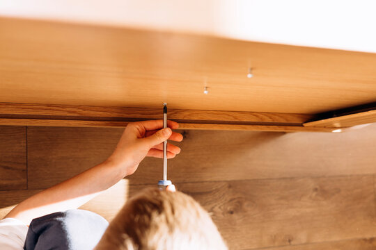 Close-up of kid's hands assembling flat pack furniture at home. DIY lifestyle scene showing home improvement, manual work, and furniture installation in natural light