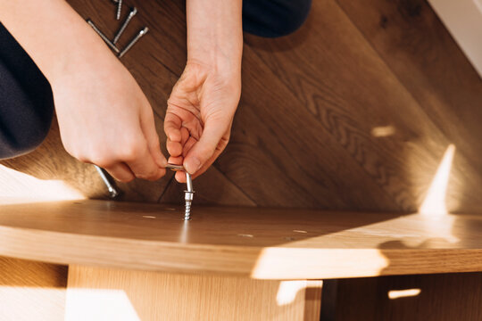 Close-up of kid's hands assembling flat pack furniture at home. DIY lifestyle scene showing home improvement, manual work, and furniture installation in natural light