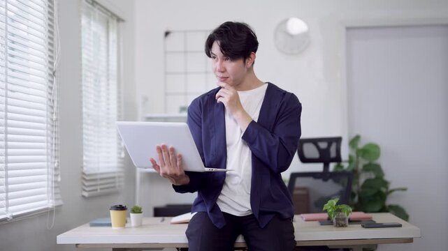 Young Asian freelancer working on laptop while sitting on desk in modern minimalist home office