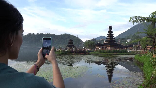 Young female traveler recording a video of the pura ulun danu beratan temple on her smartphone