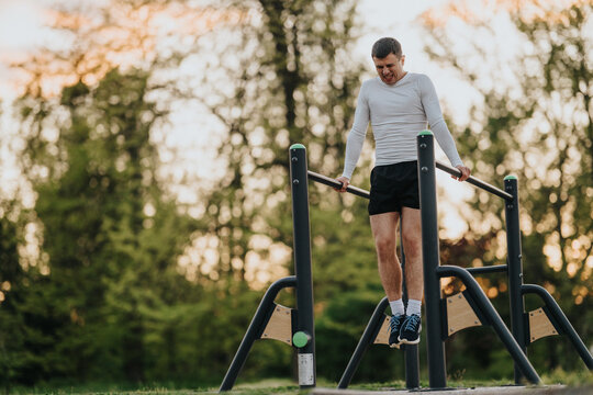 A man performs dips on outdoor parallel bars, focusing on upper-body strength. The athlete trains calisthenics on park equipment at dusk for a focused workout.