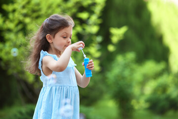 Fototapeta premium Young child creating soap bubbles outdoors, enjoying playtime in green nature during summer. Childhood joy concept