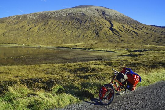 A loaded bicycle stands at the roadside in front of an impressive mountain landscape under a clear blue sky, Cycling tour, October, Hebrides, Isle of Skye, Hebrides, Scotland, Great Britain