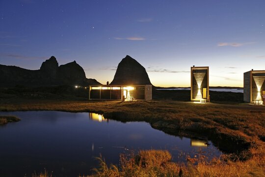 Futuristic wooden houses of a tourist accommodation and the mountain Traenastoppen at dusk, Traena, Helgelandskysten, Norway