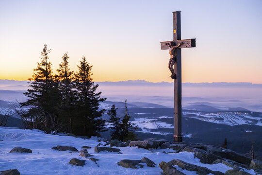 Christian cross on the peak of Mount Lusen with the view over the hills of the bavarian forest at sunrise at winter, Bavaria, Germany