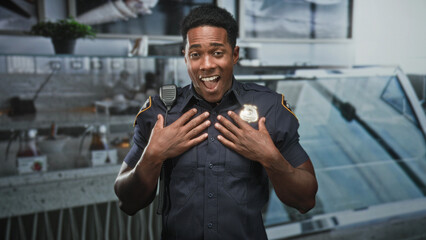 Fototapeta premium Man police officer smiles and gestures with hands near chest while displaying badge at a service counter inside a building; pride duty.