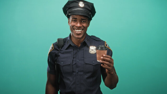 Man holding a takeaway coffee cup and smiling, police officer in uniform stands against a teal studio backdrop while raising the cup in greeting; cheerful break.