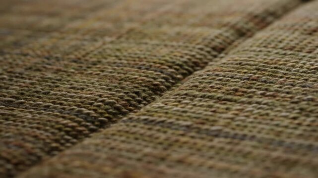 Shifting focus across chunky woven upholstery fabric reveals diagonal raised seam, dense stitch detail, earthy neutral tones, soft blur, and tactile surface texture with warm interior styling