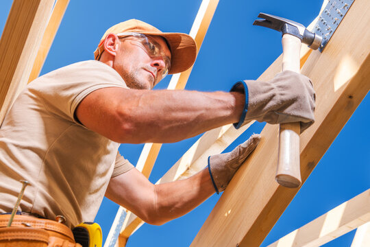 Builder works with hammer on wooden structure in bright sunlight