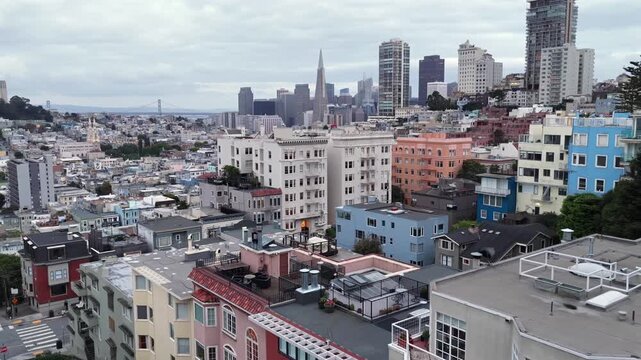 Colorful pastel apartment facades lining steep Lombard Street hill with Transamerica Pyramid and dense San Francisco skyline beyond in San Francisco, California, USA. Aerial drone backwards shot.
