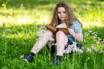 Obraz premium Kid studying outdoors feels calm and peaceful. Smart kid enjoys storytelling in nature. Focused educational kid reads vintage book. Kid portrait shows thoughtful expression.