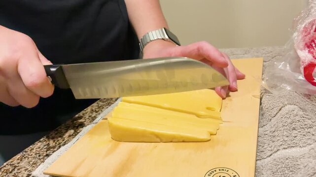 Close up of a woman's hand slicing yellow cheese with a knife on a wooden cutting board, traditional Picada Argentina