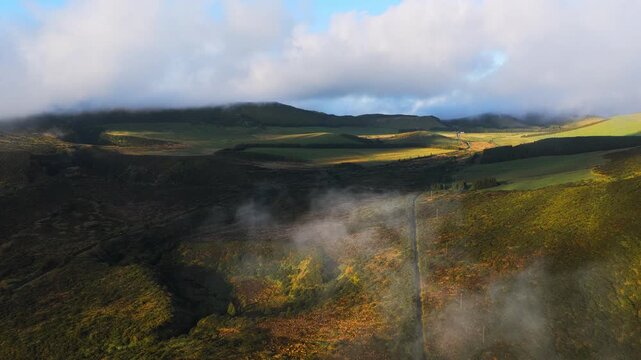 Aerial view of the lush volcanic landscape with rolling green hills and low-hanging clouds over the terrain in Faja Grande, Acores, Portugal.