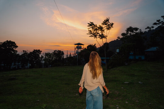 Woman Walking at Sunset Near Trees and a Tower