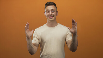 Young man in glasses holds hands apart palms facing outward showing space in orange studio  amused confidence. © Krakenimages.com