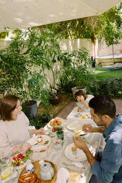 Father and mother with a toddler having breakfast in the garden
