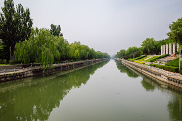 Fototapeta premium Scenic City Moat with Green Tree Reflections and Riverside Park Landscaping. A section of a canal in Beijing, China.