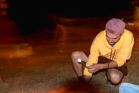 Man roasting marshmallow at night by warmth of bonfire